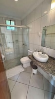 Un baño con cabina de ducha de vidrio, inodoro blanco, lavabo con encimera de granito y espejo sobre el lavabo.