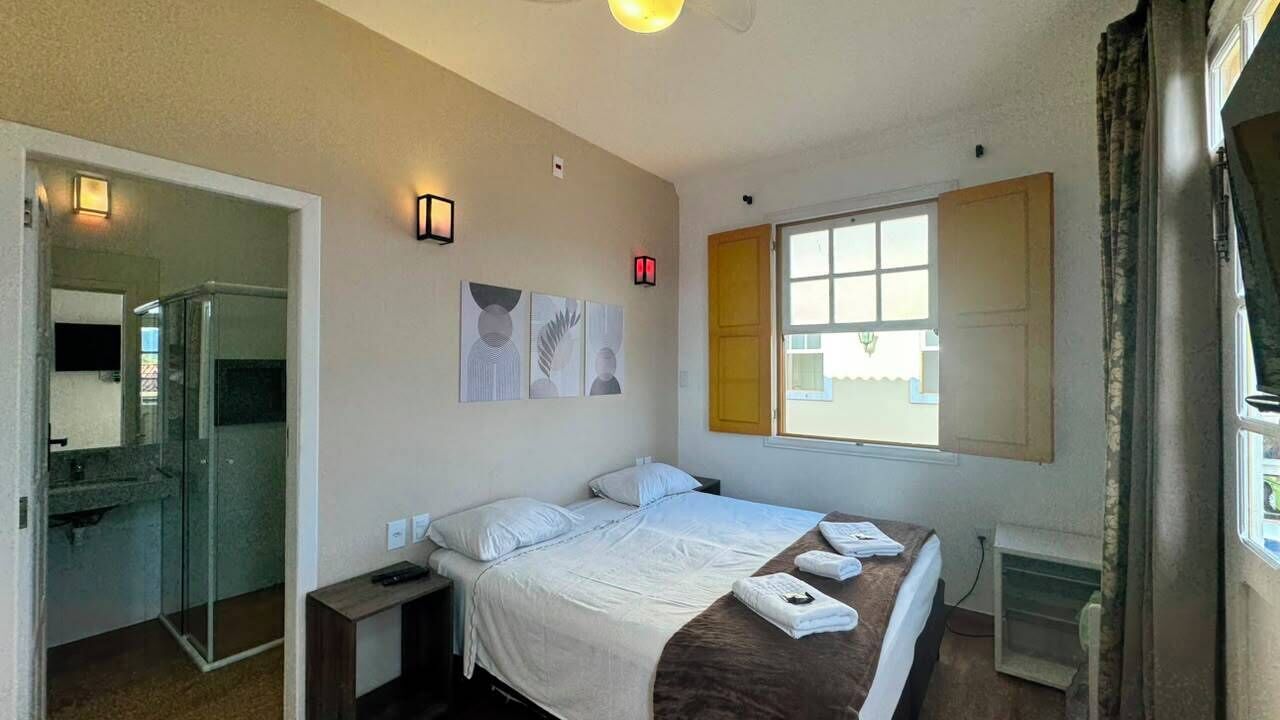 Ett hotellrum med en säng, sängbord, en dusch och ett fönster med gardiner.