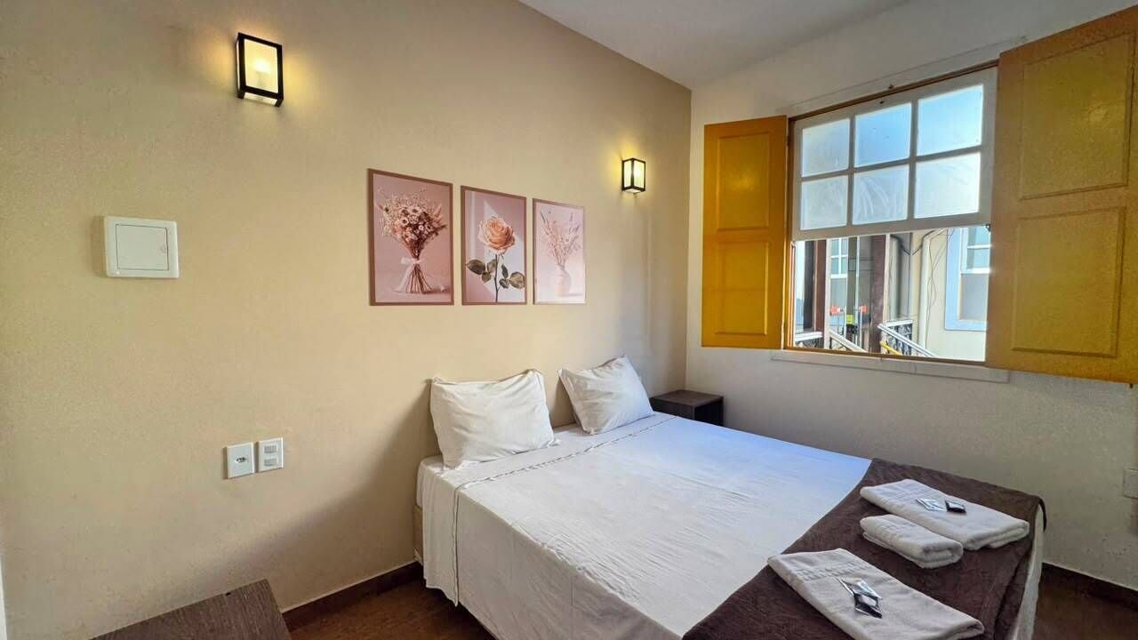 A bedroom with a bed, a bedside table, a window, and wall-mounted light fixtures.
