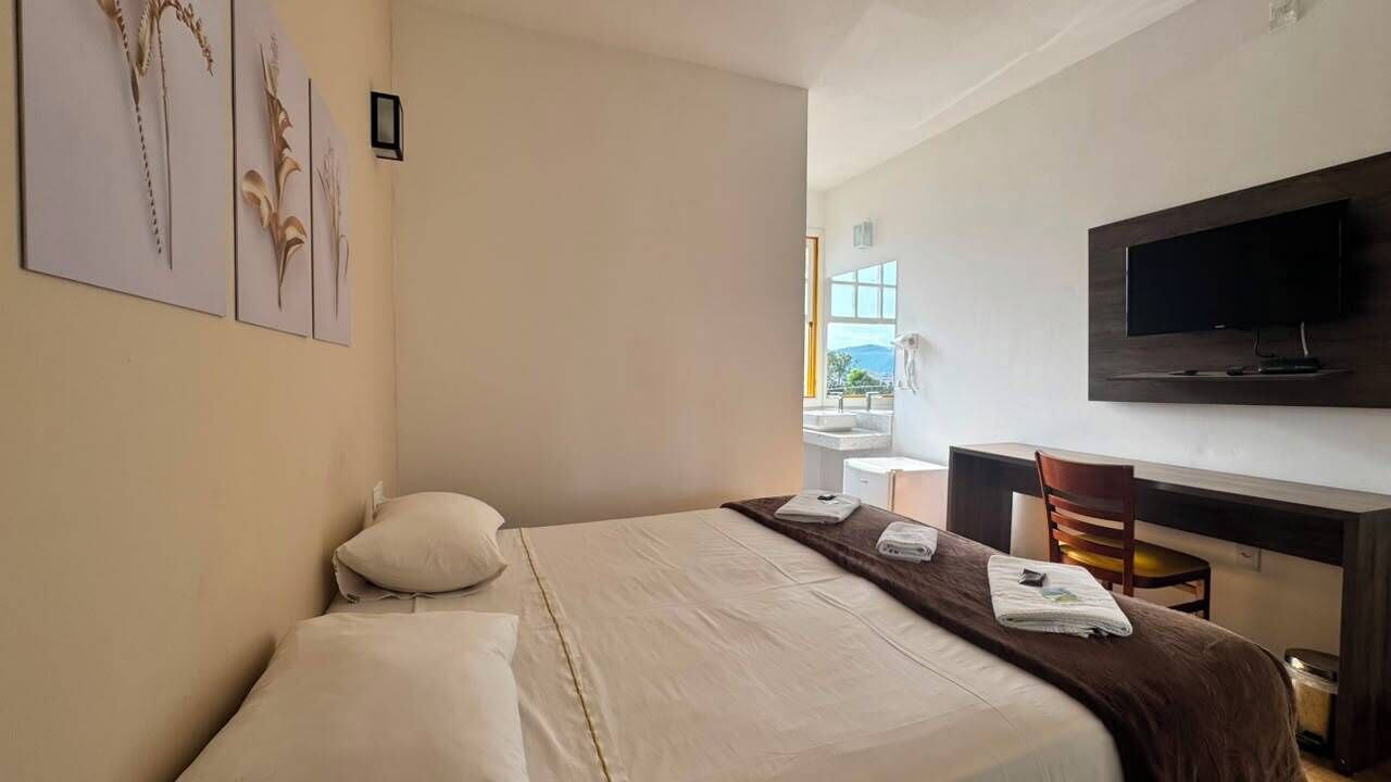 A hotel room with a bed, a desk, a television, and artwork on the wall.