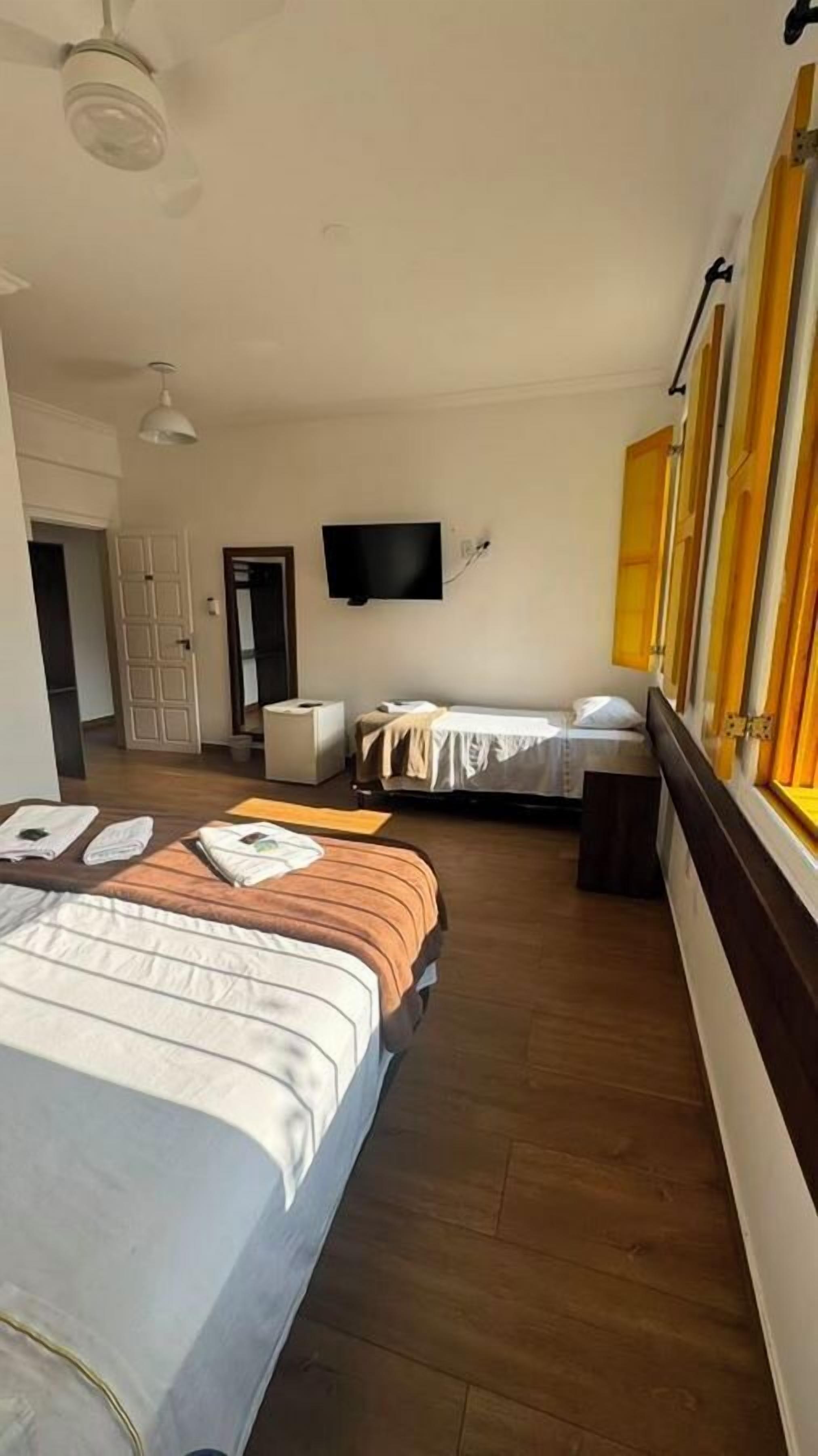A hotel room with two beds, a television, and a window with curtains.