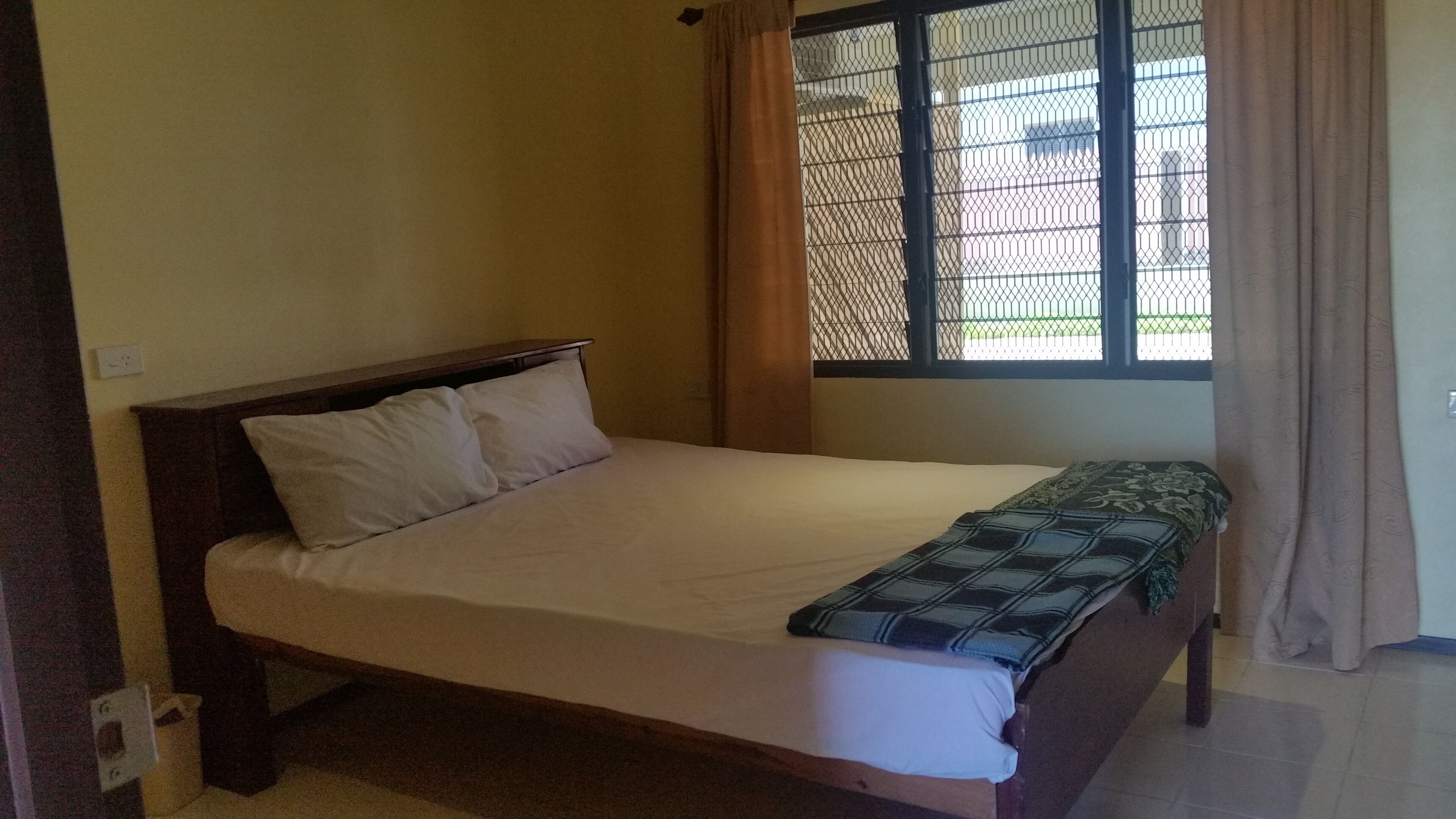 A single bed with a wooden headboard, a white mattress, and a plaid blanket.