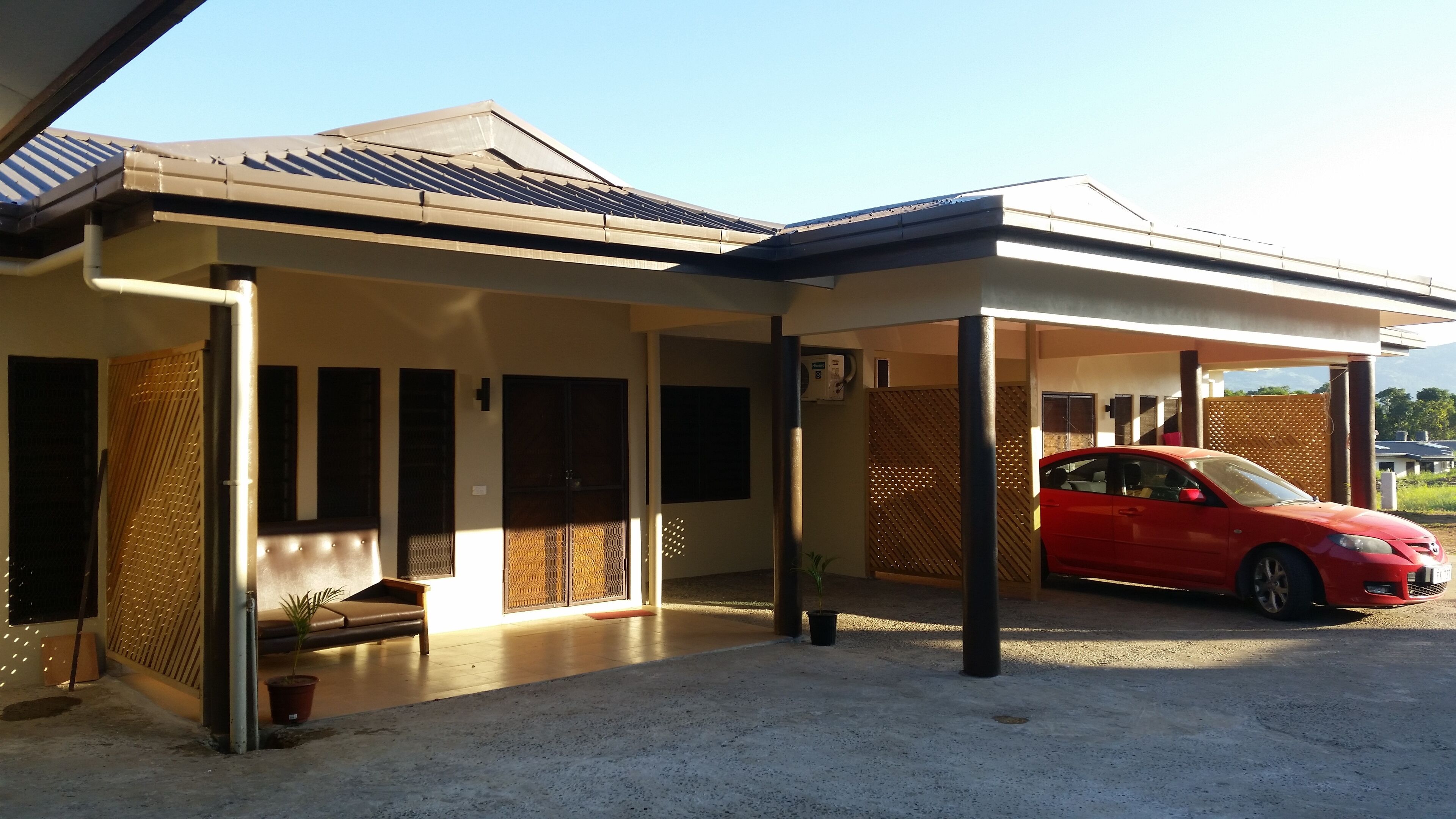A modern building with a covered parking area, a red car parked inside, and a small seating area with a bench and potted plants.