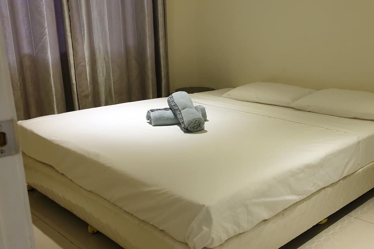 A neatly made bed with white linens and a rolled towel on top.