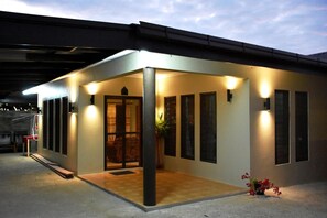 A modern building with a covered entrance, large windows, and a small garden area with flowers. - Westfield Homestay Fiji (Nadi)