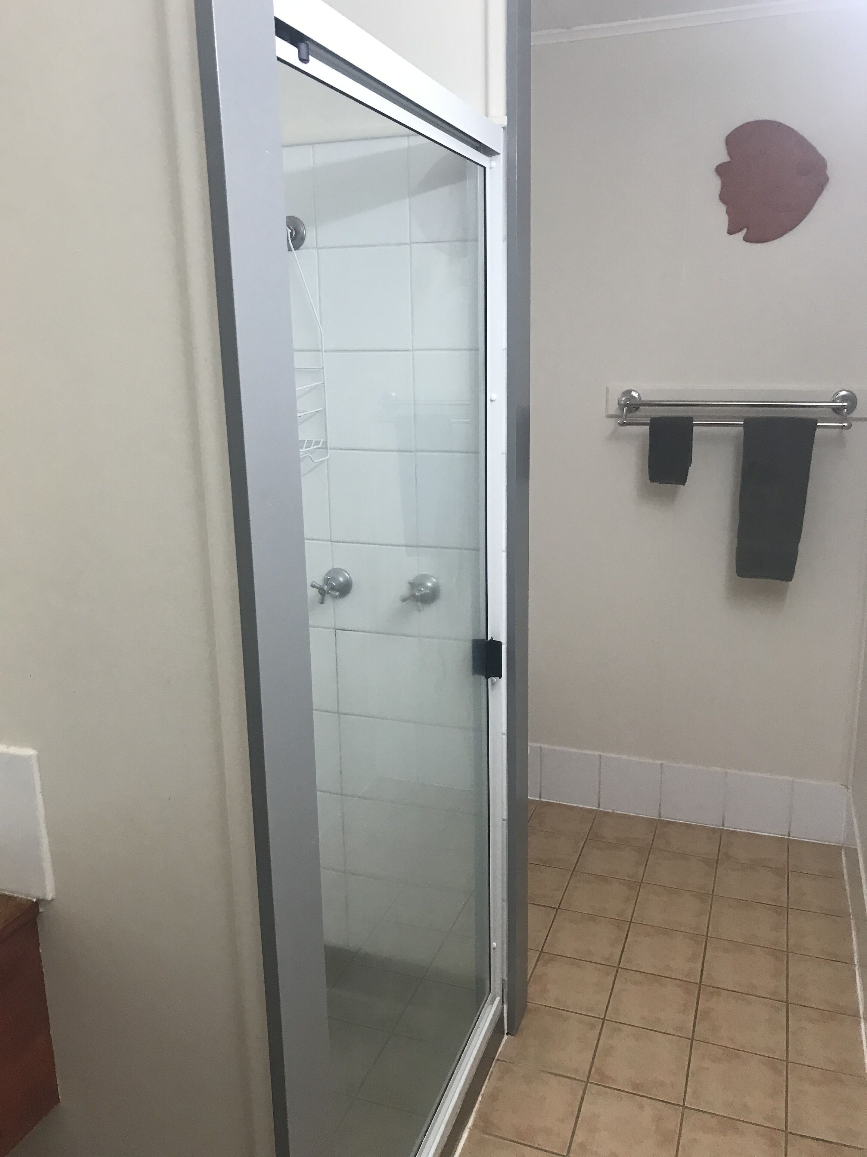 A bathroom with a glass shower door, a towel rack, and a tiled floor.