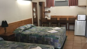 Een kamer met twee bedden, een klein kitchenette, een houten bureau en een spiegel.