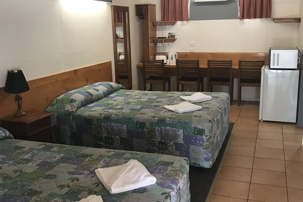 A room with two beds, a small kitchenette, a wooden desk, and a mirror.