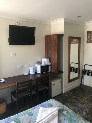 Une chambre d’hôtel équipée d’un lit, d’un bureau avec un micro-ondes, d’une télévision, d’un petit réfrigérateur et d’un miroir.