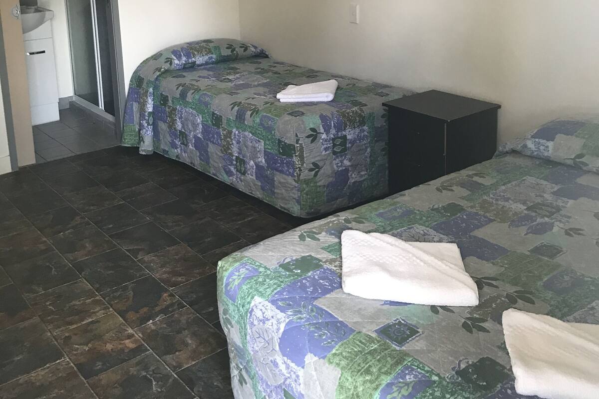 A bedroom with two beds, a bathroom, and an air conditioning unit.