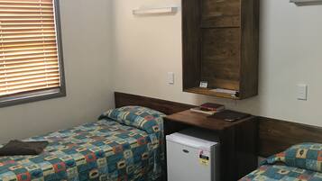 A room with two beds, a small refrigerator, a wooden wardrobe, and a window with blinds.