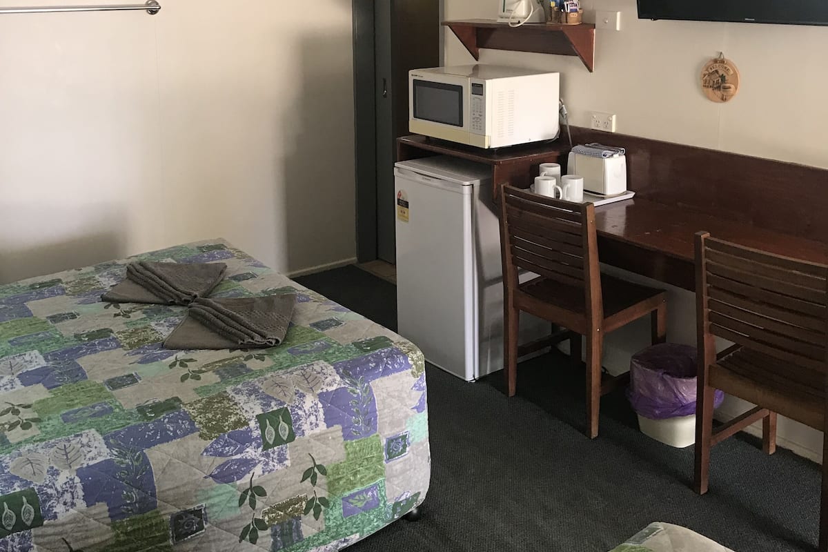 A compact hotel room with a bed, a small desk with a computer and a microwave, a TV, and a refrigerator.