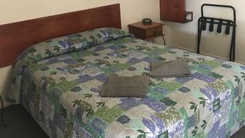 A bedroom with a bed, a wooden headboard, a small bedside table, a hanging coat rack, and a wall-mounted towel rack.
