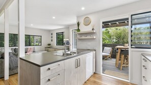 Una cocina moderna con una isla grande, un comedor con mesa y sillas de madera, y un cerramiento de vidrio corredero que da a un patio exterior con plantas.
