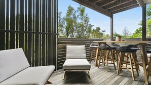 Un espacio de estar al aire libre cubierto con una terraza de madera, un sofá acolchado y taburetes de bar de mimbre.
