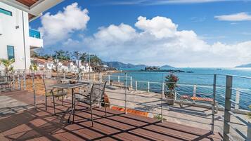 Una terraza con mesa y sillas, con vista a una zona costera con edificios y cielo despejado.
