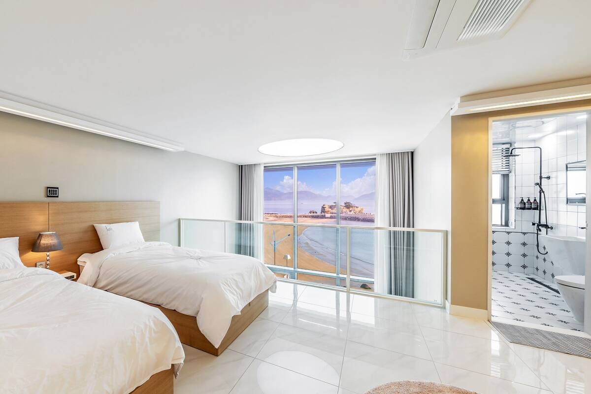 Et hotelværelse med to senge, en balkon med udsigt til stranden og et moderne badeværelse.