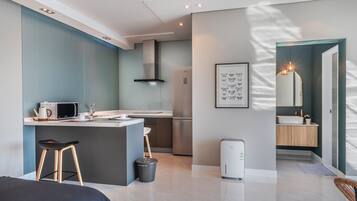 A modern kitchen with a microwave, kettle, and sink, a small dining area with stools, and a compact refrigerator.
