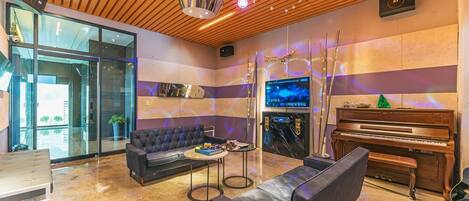 Una sala de estar moderna con sofá, sillones, una mesa de centro, un piano y una pantalla de televisión.