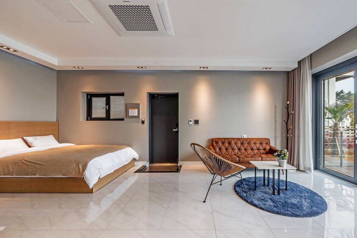 Et moderne hotelværelse med en seng, et siddeområde med stol og bord, en dør og et stort vindue med udsigt.