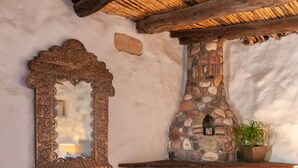 Una habitación rústica con chimenea de piedra, un sillón de fibra natural, un tablero de ajedrez y un espejo en la pared.