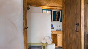 Un interior rústico con una puerta de madera que da a una zona de cocina, una mesita con toallas y una silla de mimbre.