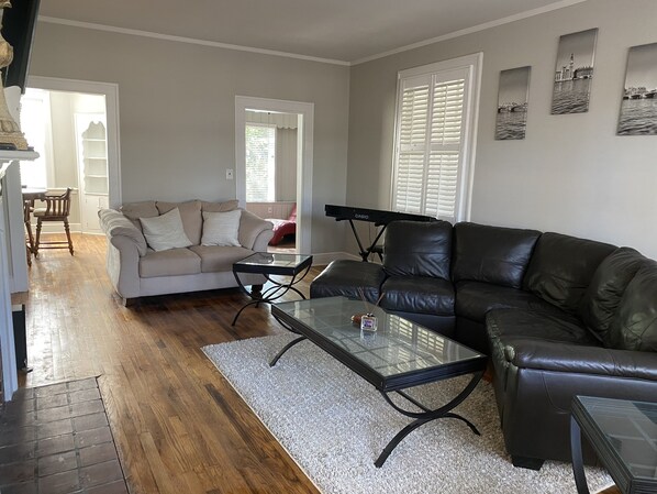 Un salon avec un canapé beige, un divan en cuir noir, une table basse en verre et un piano.