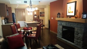 A modern living room with a fireplace, a dining area, and a kitchen in the background. - Kananaskis Getaway, 1Br. Condo in the mountains (Dead Man's Flats)