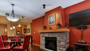 A living room with a stone fireplace, red walls, a dining area with red chairs, and a flat-screen TV mounted on the wall. - Kananaskis Getaway, 1Br. Condo in the mountains (Dead Man's Flats)