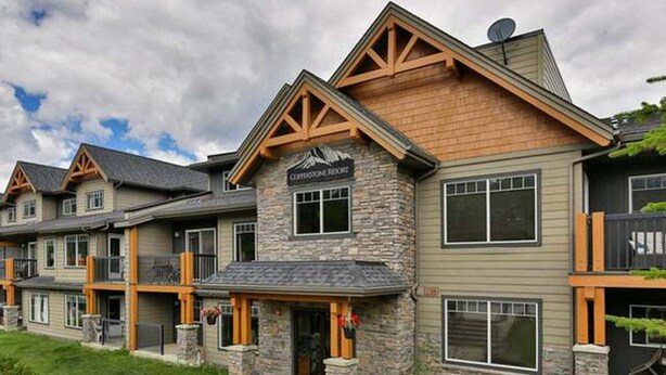 A row of modern, multi-story buildings with stone and wood accents, featuring a prominent entrance with a sign. - Kananaskis Getaway, 1Br. Condo in the mountains (Dead Man's Flats)