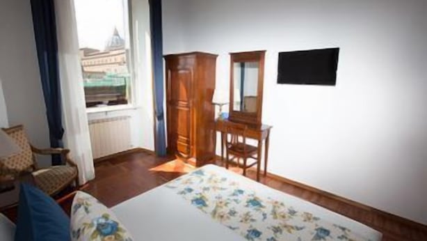 A bedroom with a bed, a desk, a chair, a wardrobe, and a window with a view of a building. - Ad 2015 Guesthouse (Rome)