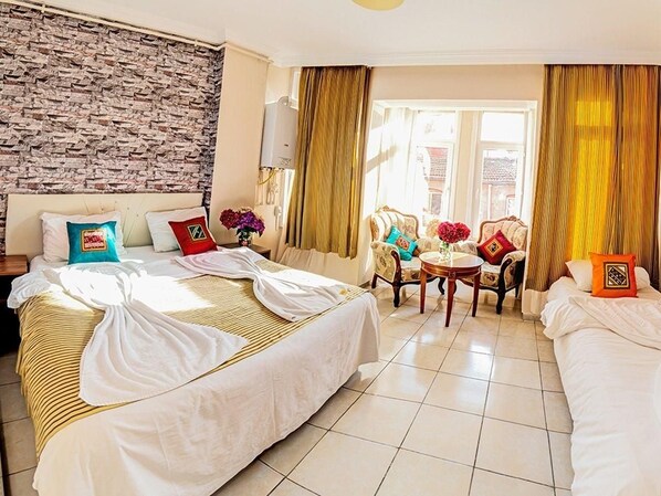 A hotel room with two beds, a brick wall, a window with curtains, and a small table with a vase of flowers.