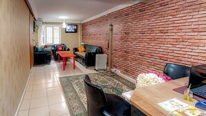 A living room with a brick wall, a TV, a radiator, and a dining area with a table and chairs. - White Palace Apart (Istanbul)