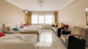 A hotel room with two beds, a sofa, a chair, a small table, and a window with curtains.