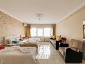 A hotel room with two beds, a sofa, a chair, a small table, and a window with curtains.