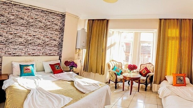 A hotel room with two beds, a brick wall, a window with curtains, and a small table with a vase of flowers. - White Palace Apart (Istanbul)