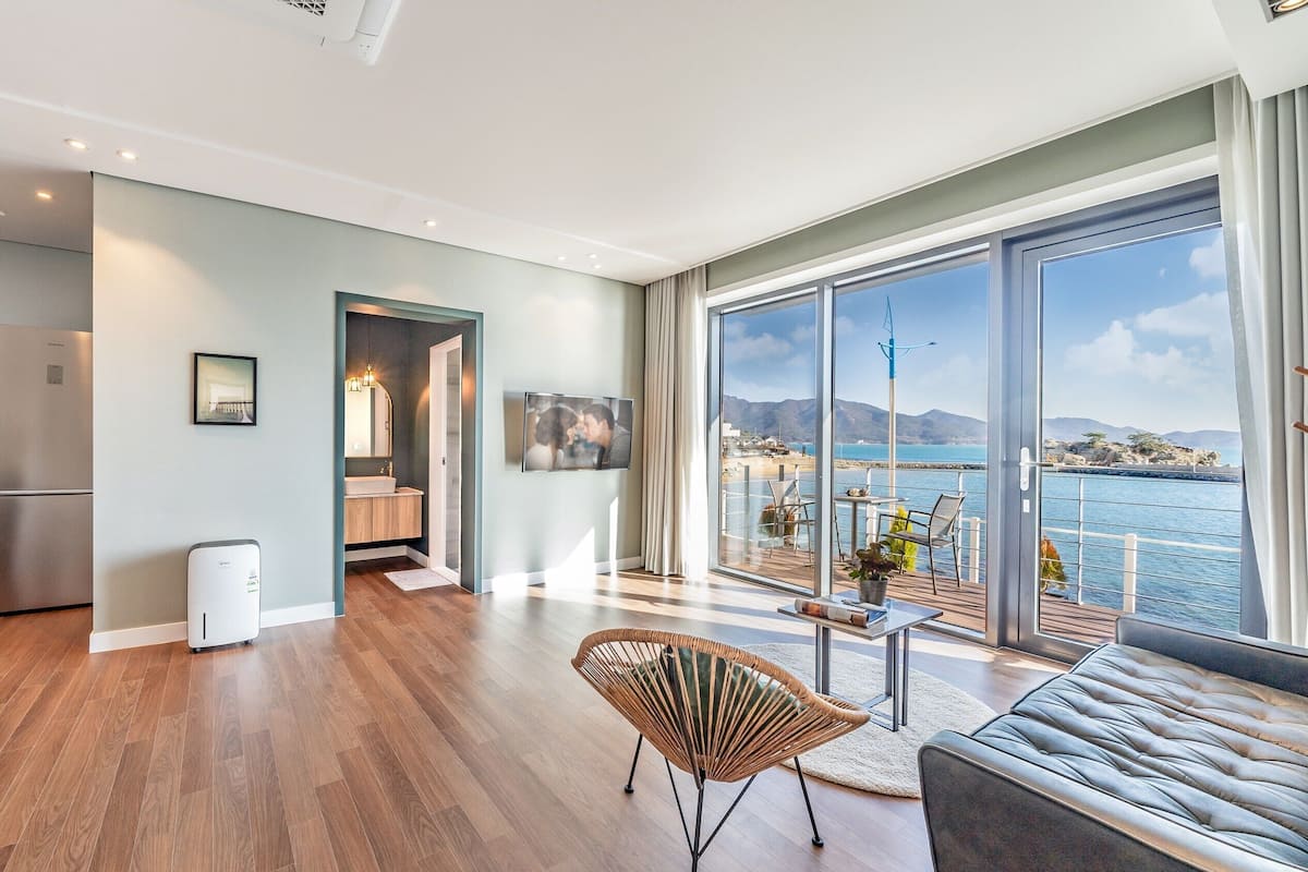 A modern living space with a kitchen, dining area, and a balcony with a view of the sea.