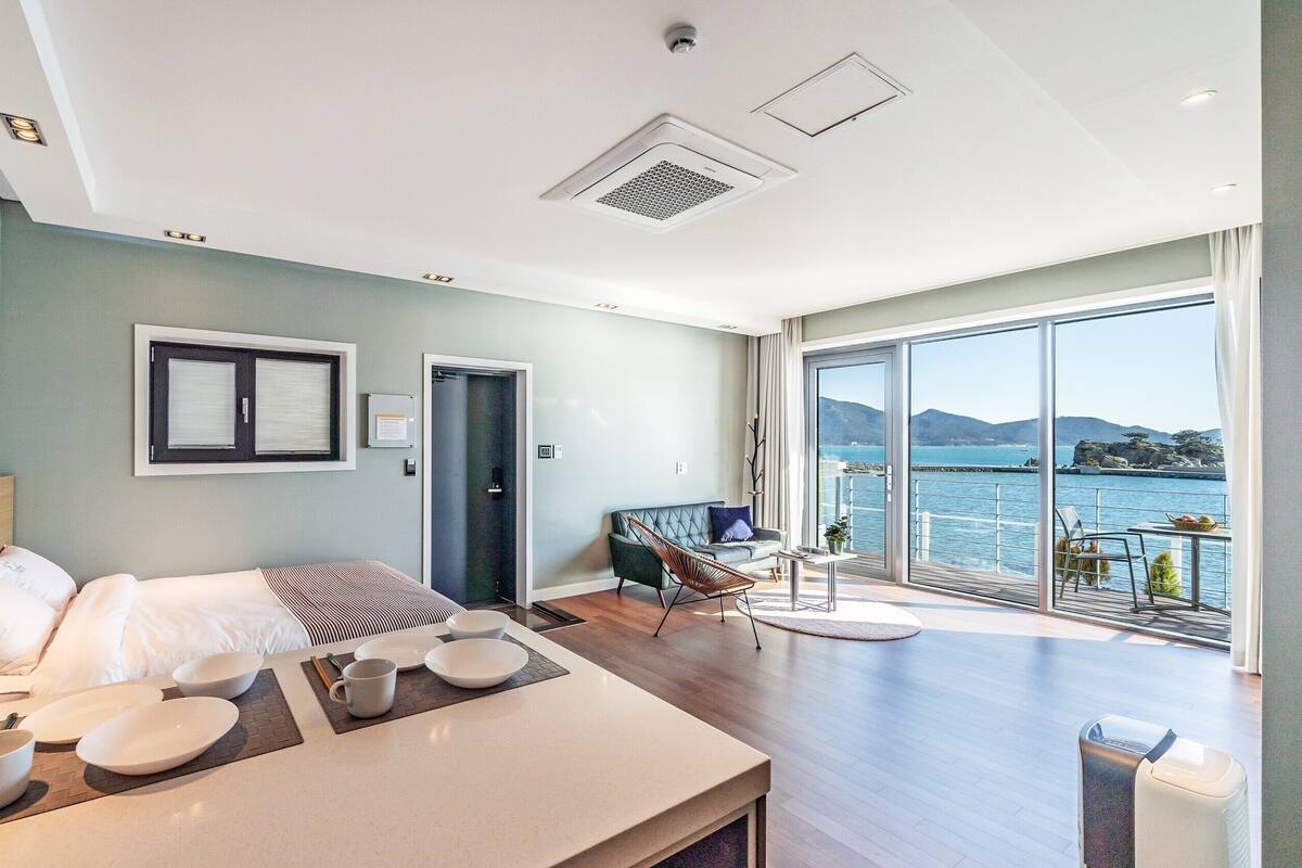 A modern hotel room with a bed, bedside table, and a view of the sea.