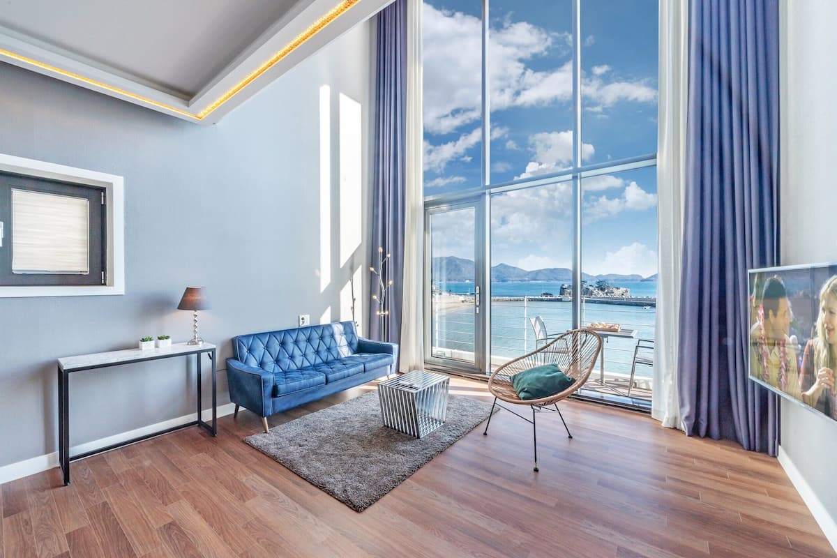 A modern living room with a large window offering a view of the sea and mountains.