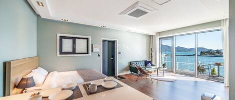 A modern hotel room with a bed, a dining area, and a balcony with a view of the sea.