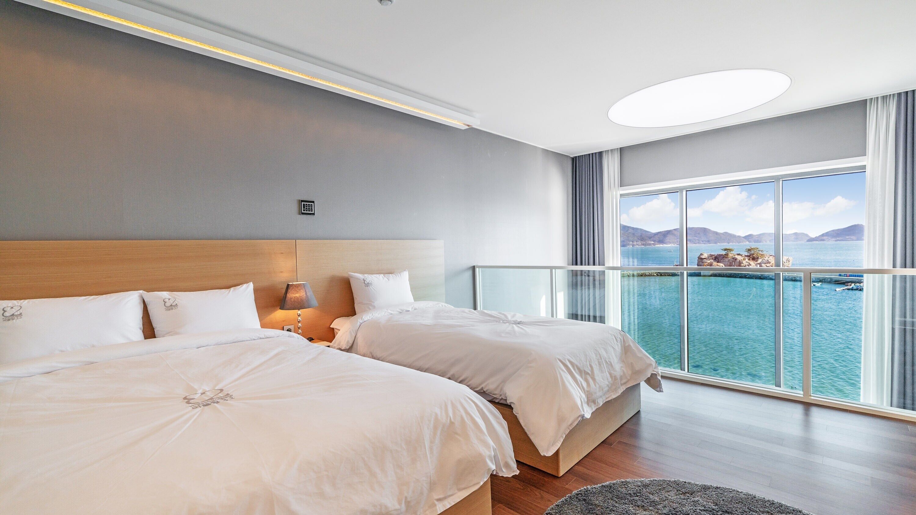 A hotel room with two beds, a large window with a view of the sea, and a modern design.