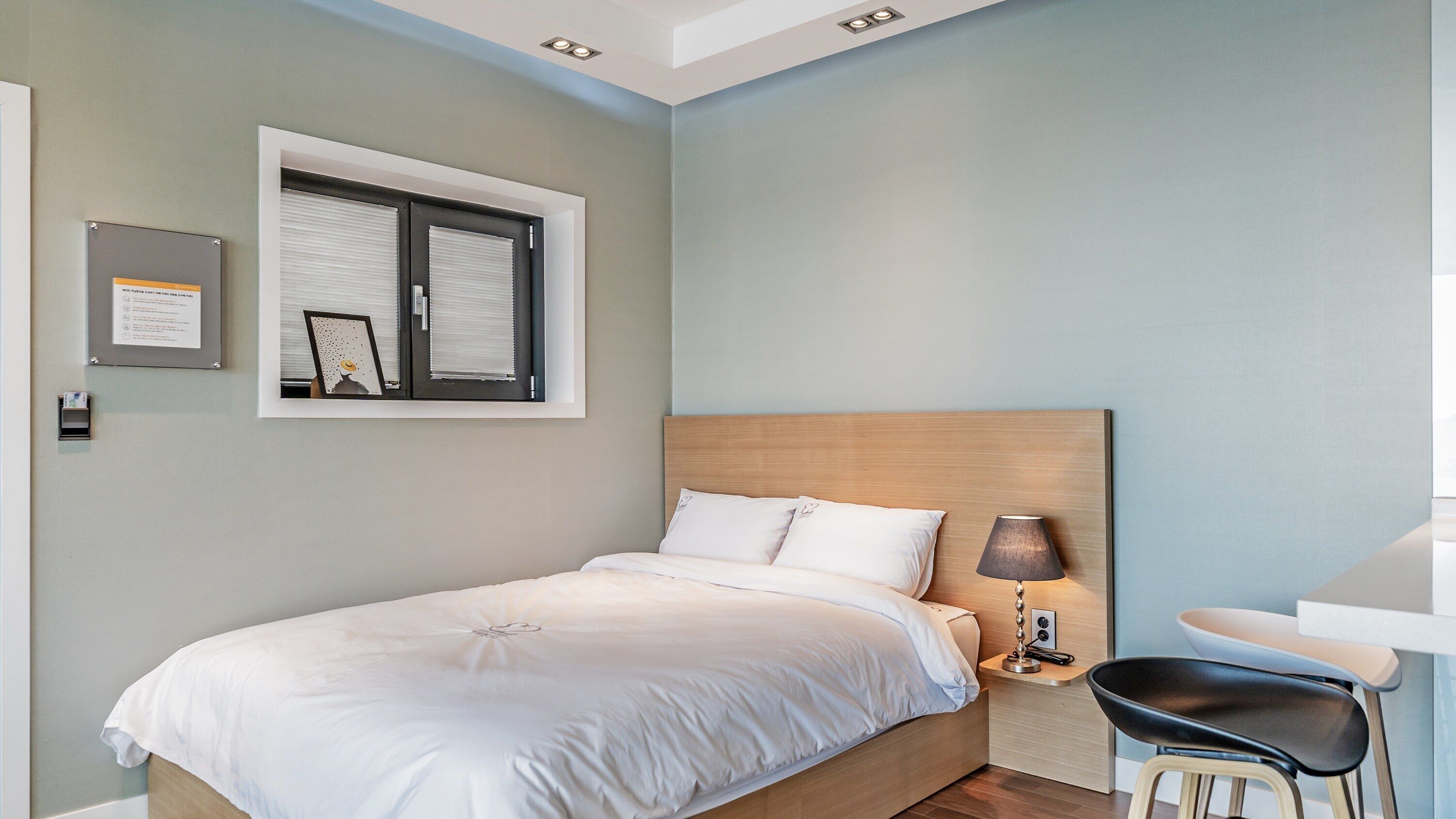 A neatly arranged hotel room with a bed, a desk, a chair, and a lamp.