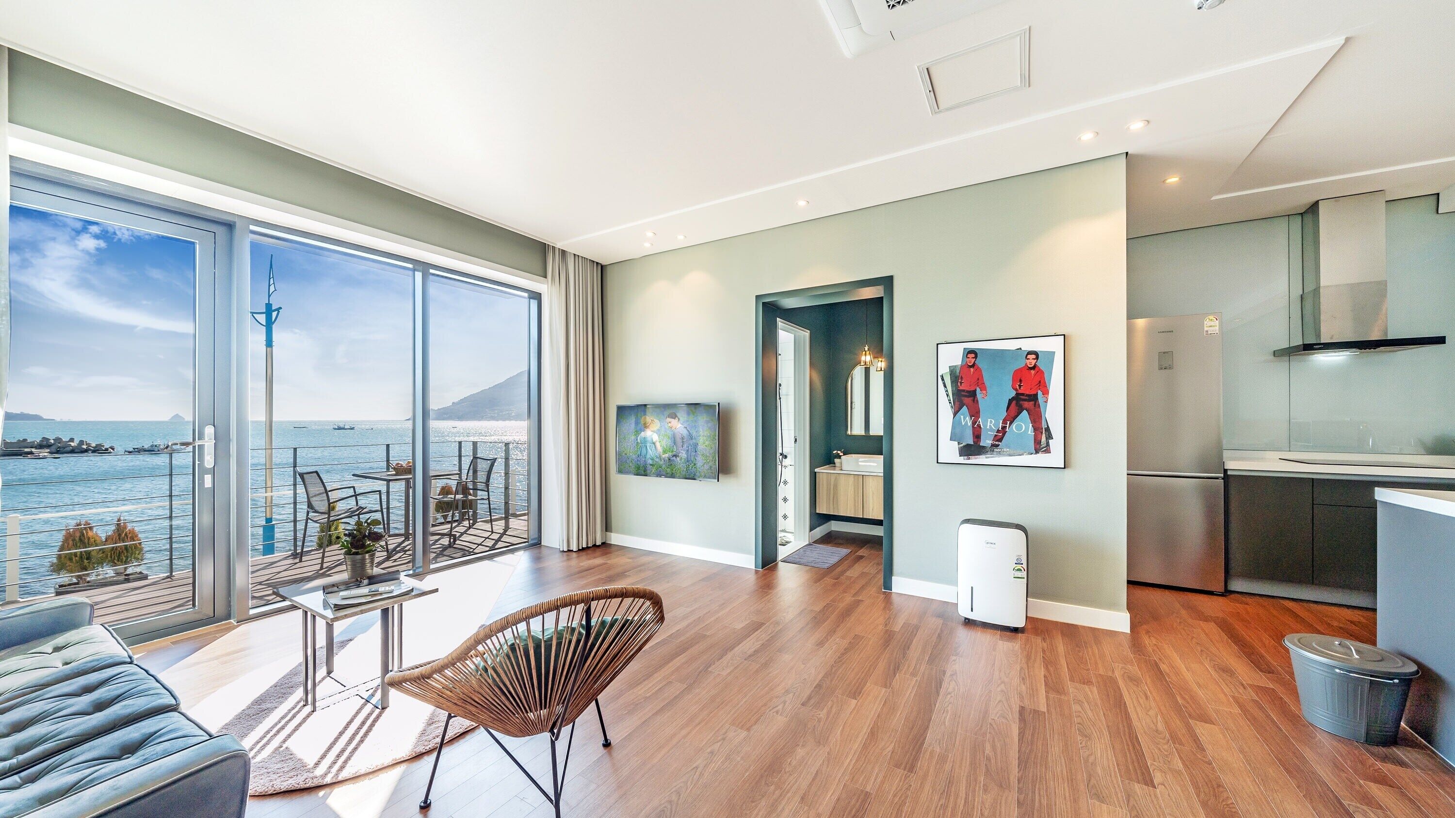En rummelig opholdsstue med stor balkon og udsigt over det naturskønne hav, et moderne køkken og et spiseområde med havudsigt.