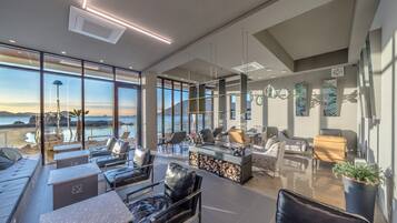 A modern lounge area with leather chairs, a bar, and large windows offering a view of the sea.