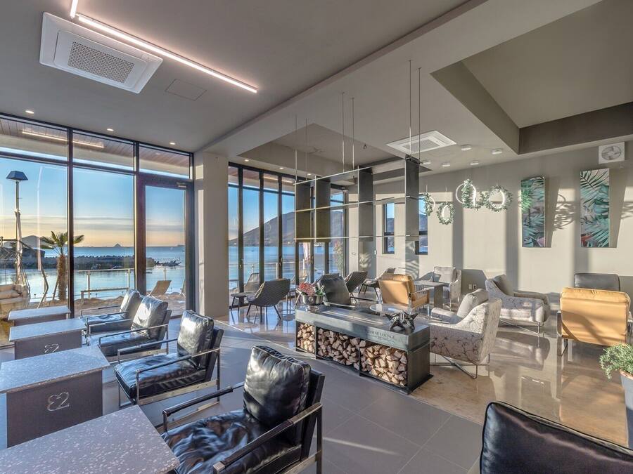 A modern lounge area with leather chairs, a bar, and large windows offering a view of the sea.