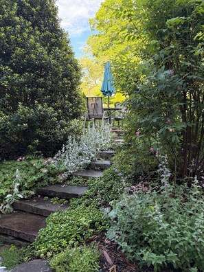 Un jardin avec des marches en pierre, une chaise en métal et un parasol bleu.