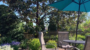 Eine Terrasse mit Backsteinboden, Metallstühlen, einem Tisch und einem grünen Sonnenschirm.