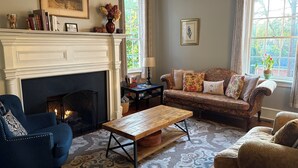 Ein gemütliches Wohnzimmer mit Kamin, einem blauen Sessel, einem gemusterten Sofa und einem Couchtisch.