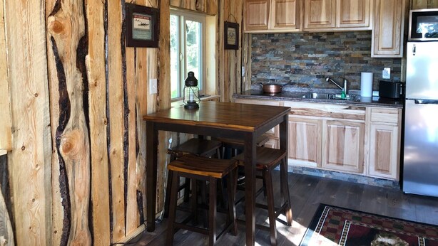 A rustic kitchen with wooden cabinets, a stone backsplash, and a stainless steel refrigerator. - CAM'S LAKESIDE BUNKHOUSE  (Soldotna)