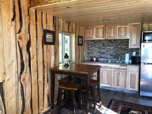 A rustic kitchen with wooden cabinets, a stone backsplash, and a stainless steel refrigerator. - CAM'S LAKESIDE BUNKHOUSE  (Soldotna)